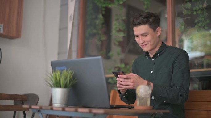 笑容可掬的专业年轻亚裔中国商人在室外咖啡馆露台上使用笔记本电脑