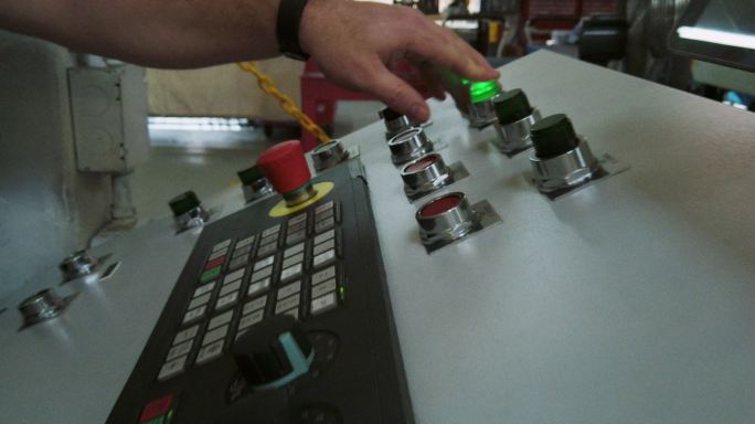 一位30多岁的白人技师在室内制造设施中按下按钮和控制装置