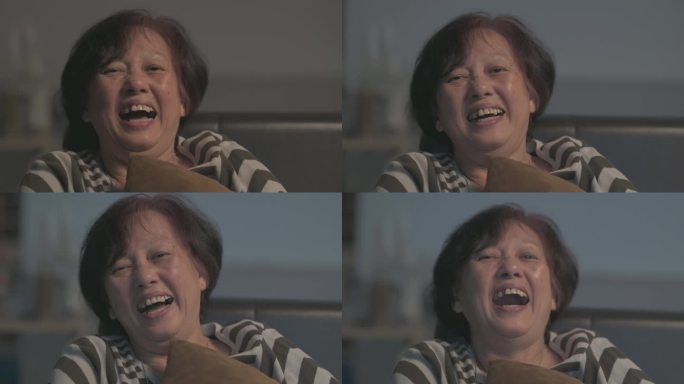 font-view亚洲华裔高龄女性在周末休闲时间喜欢在家看电视，晚上独自一人在喜剧电视剧中大笑