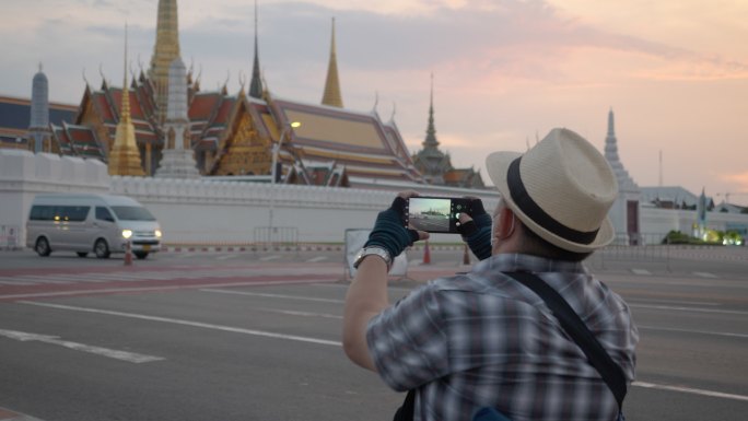 曼谷概念轮椅旅游地标。坐轮椅的游客使用手机拍摄大皇宫（Wat Phra Kaew），并使用平板电脑。