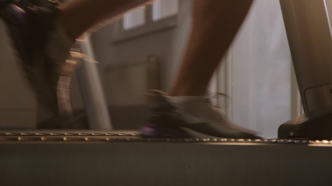 在晨曦中，特写健身房跑步机上跑步的运动双脚。