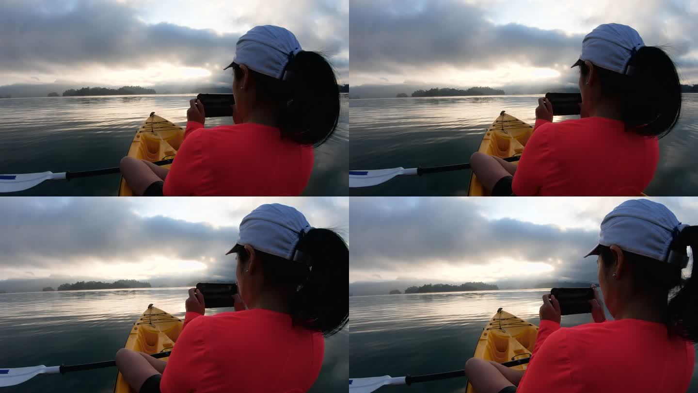 亚洲女子在热带大湖划船并使用手机拍摄日出照片