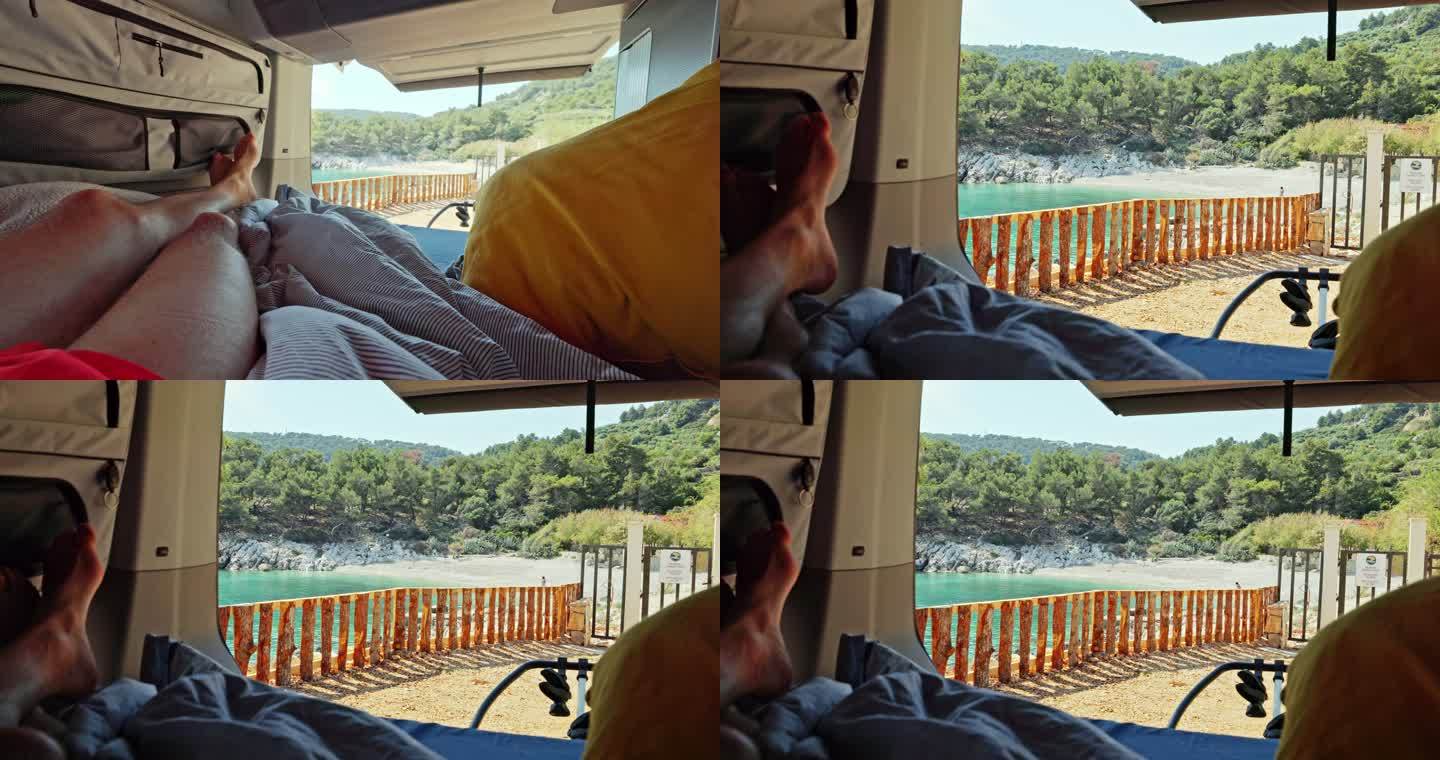 男子躺在货车的床上，货车后门打开，背景是美丽的海滩