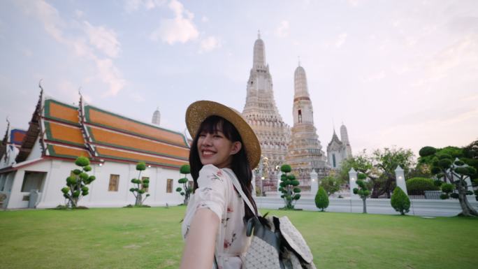 在曼谷Wat Arun，一位快乐的亚洲年轻女子牵着男友的手旅行