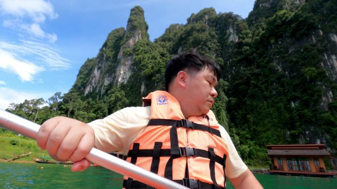 一名身穿救生衣的亚洲男子在湖中学习皮划艇