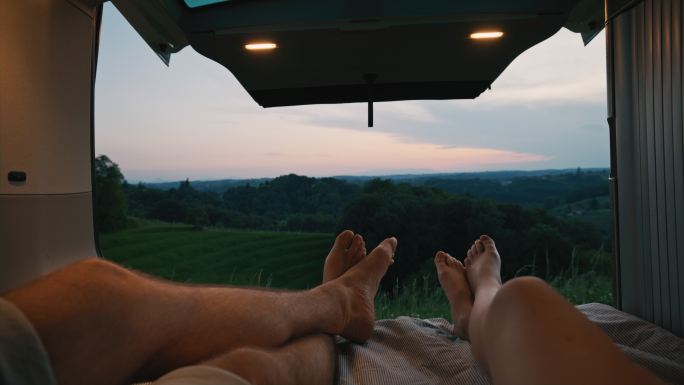远景：黄昏时分，一对年轻夫妇的脚在乡村某个地方的一辆货车后面