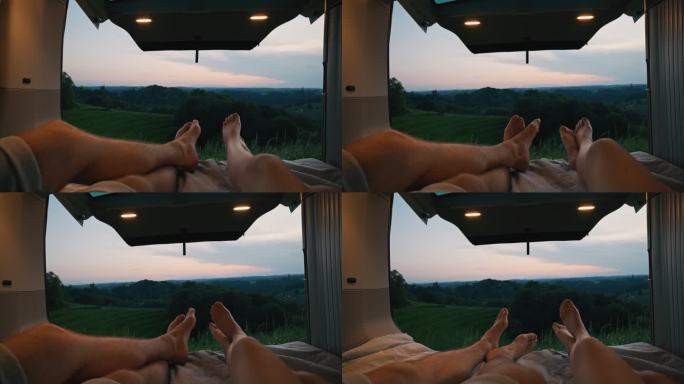 远景：黄昏时分，一对年轻夫妇的脚在乡村某个地方的一辆货车后面