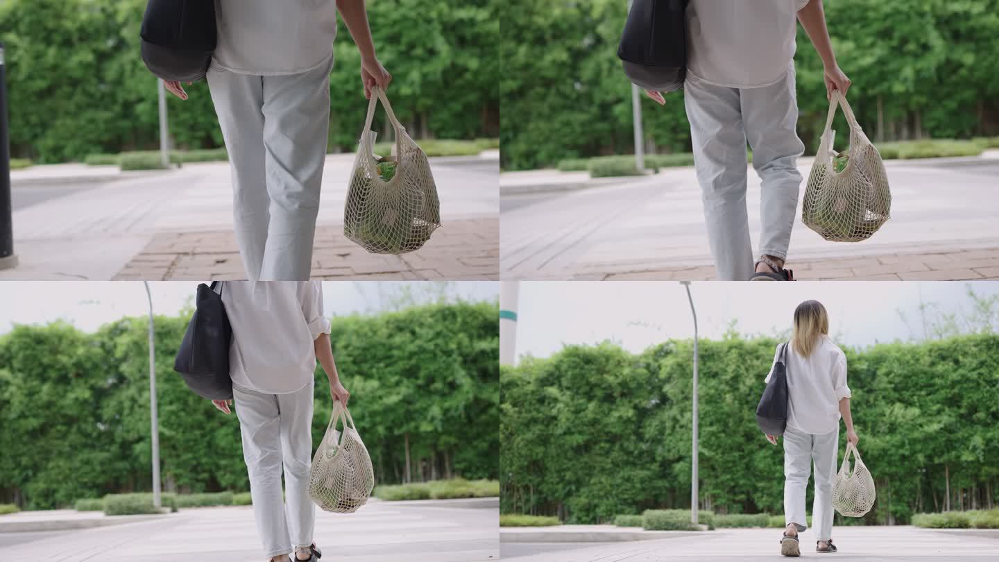 穿着休闲服的年轻女子手持可重复使用的网袋穿过绿色城市场景中的道路