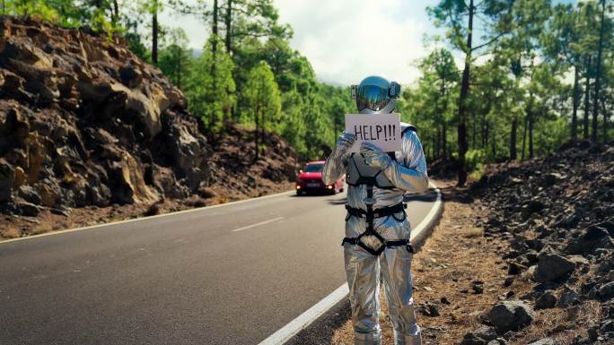 失踪的宇航员正在寻求帮助。在山路上搭便车。手持“帮助”标志