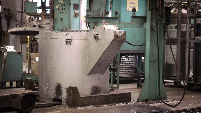 铝熔炼，操作员努力将钢包中的熔融金属敲入保温炉压铸机