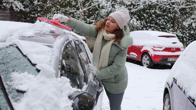 一位年轻女子正在清理汽车上的积雪