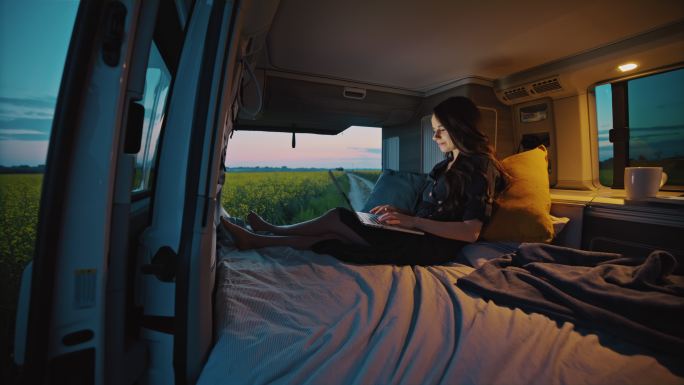 黄昏时分，DS Woman在乡村露营车的驾驶室里使用她的智能手机和笔记本电脑