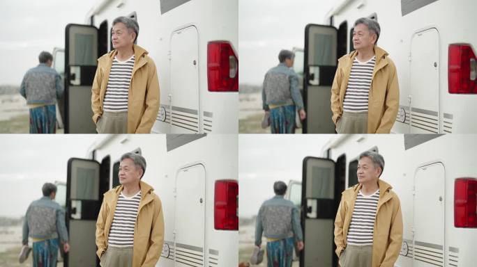 一位穿着风衣的亚裔中国老人看着停在海滩上的房车前