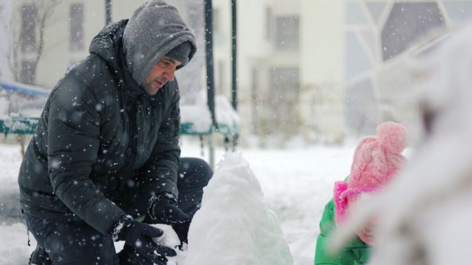 爸爸和他的孩子们在后院玩雪球，爸爸和他的女儿们在外面玩雪球。爸爸和女儿们在堆雪人，两个姐妹在雪地里玩