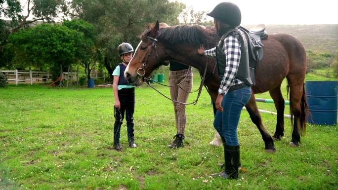女教练和女孩们在草地上放牧棕色的马