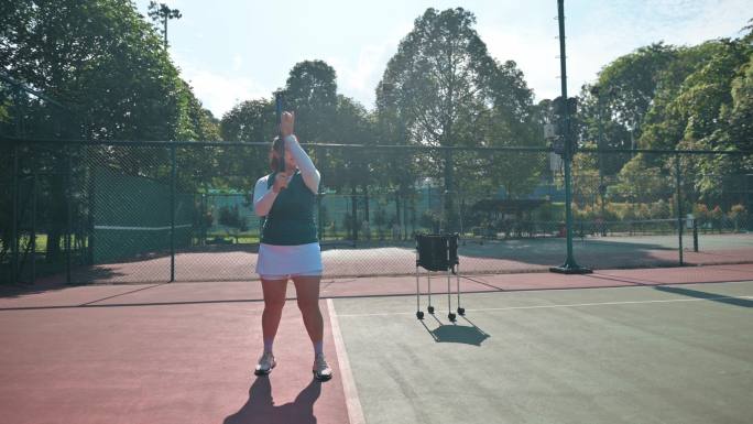 周末上午，中国亚裔女子在网球场练习发球