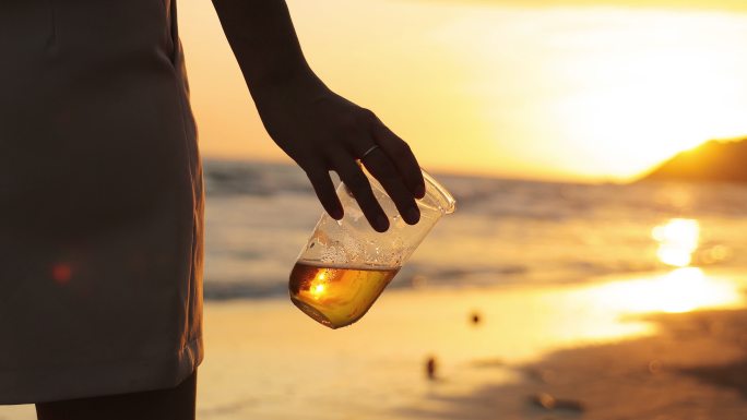 在美丽的日落中，年轻女性在海边喝啤酒，形成剪影