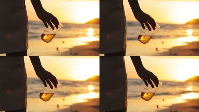 在美丽的日落中，年轻女性在海边喝啤酒，形成剪影