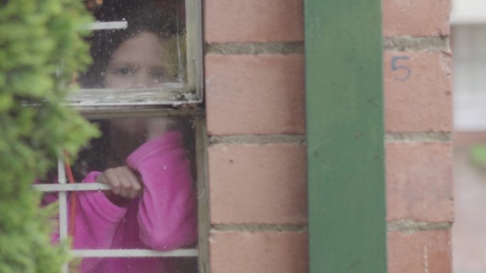 一个拉丁女孩在家里看着雨从窗户落下