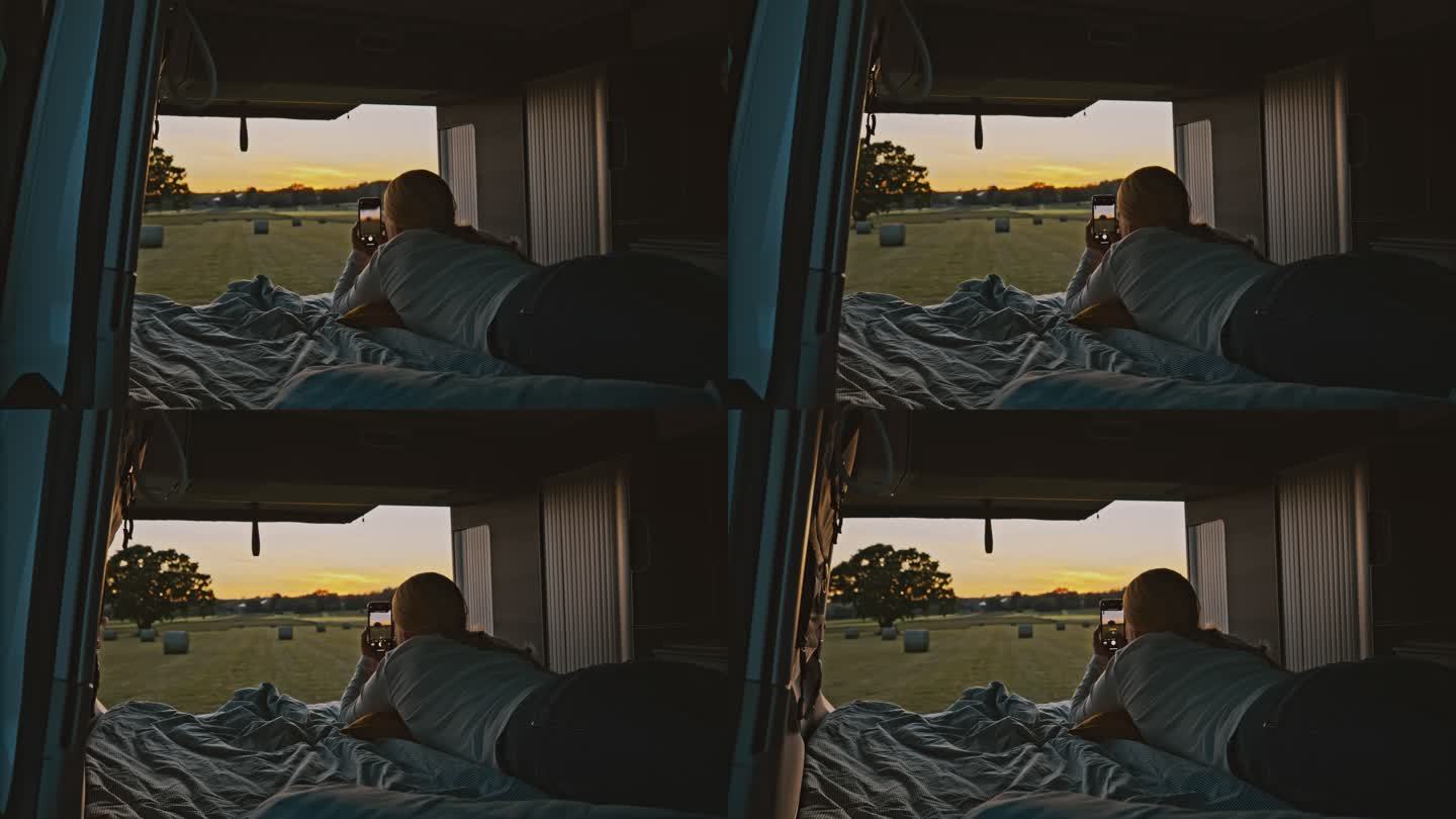 DL Woman在日落时分停在草地上的一辆露营车的小屋里用手机拍照