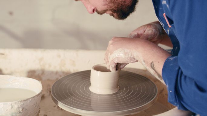 一个专业的男性陶工的手在车间里制作陶罐。富有创造力的年轻人，以他最喜爱的雕刻爱好享受闲暇时光，认真练