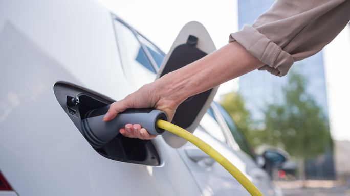 有环保意识的女性将电动汽车连接到商业区的电动汽车充电站