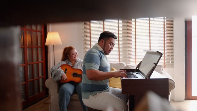 一对年轻的亚洲夫妇在公寓里作为音乐家一起弹钢琴和吉他