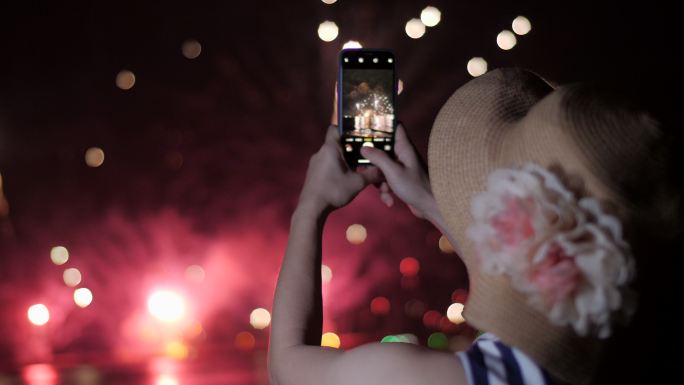女人用手机拍烟火照片。天空背景上的轮廓照亮了烟花