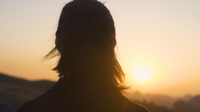 女生山顶眺望夕阳逆光剪影风吹头发登高望远