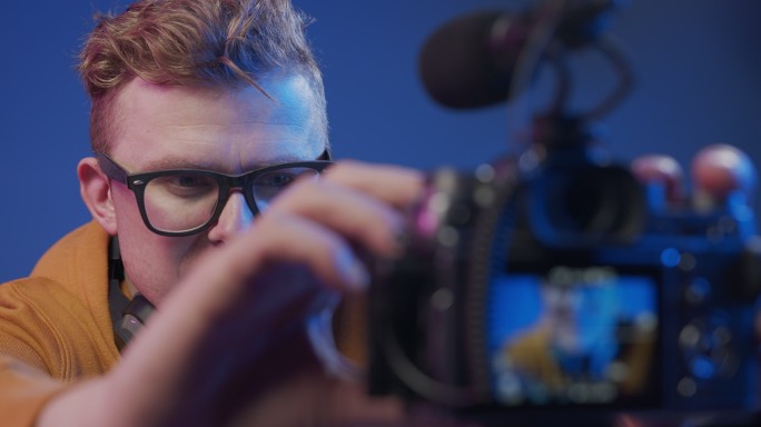 一位年轻的金发碧眼的博主戴着眼镜，为拍摄设置了相机设置