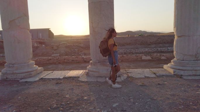 日落时分，在帕穆卡勒的莱卡斯岛上，一位旅游摄影师女孩手持相机，走在柱子后面