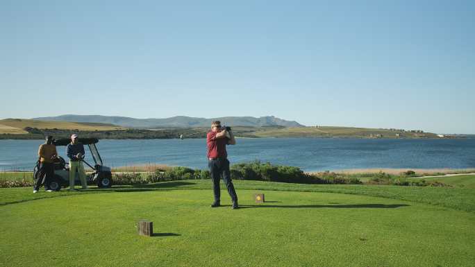 男高尔夫球手在阳光明媚的湖畔高尔夫球场发球箱上发球