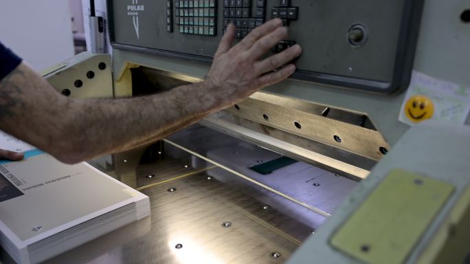印刷厂中无法辨认的工人在CNC切割机上切割一捆纸的特写镜头