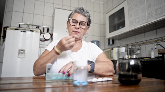 一位年长的女士看着手表，然后从每日药片组织者那里拿了一片药片，并用一口水吞下