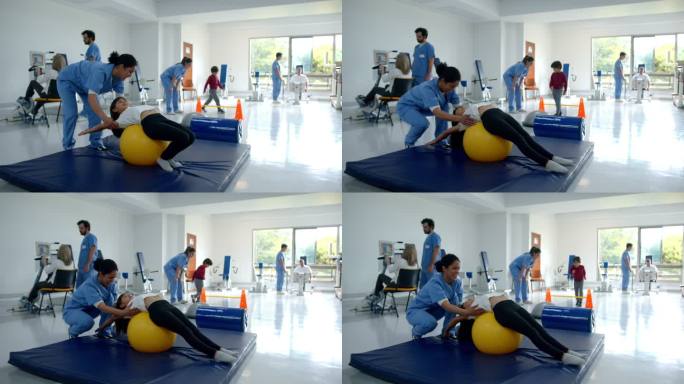 在物理康复中心的物理治疗师的帮助下，年轻女孩在健身球上伸展背部