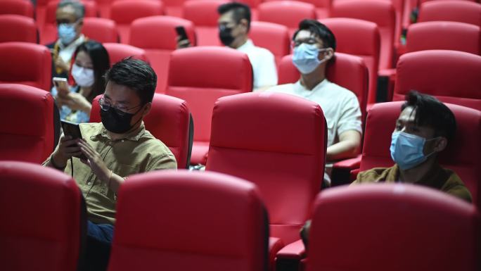 亚裔华人混合年龄组的人坐在电影院里用智能手机等待电影放映时间