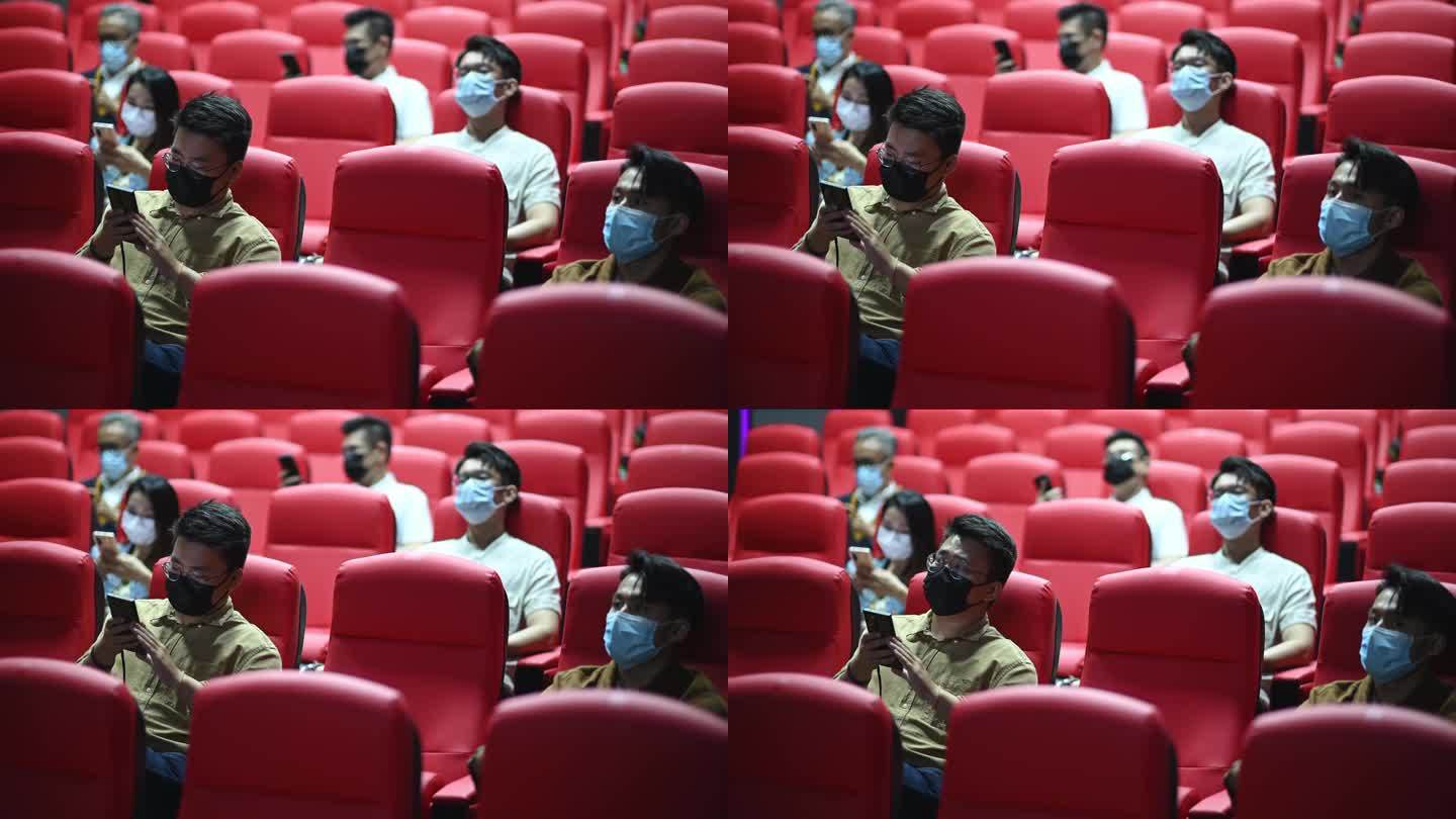 亚裔华人混合年龄组的人坐在电影院里用智能手机等待电影放映时间