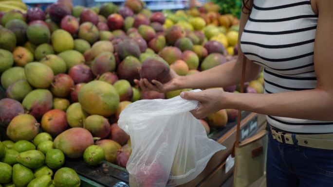 特写镜头：一位不知名的女士从零售店挑选水果并将其放入塑料袋