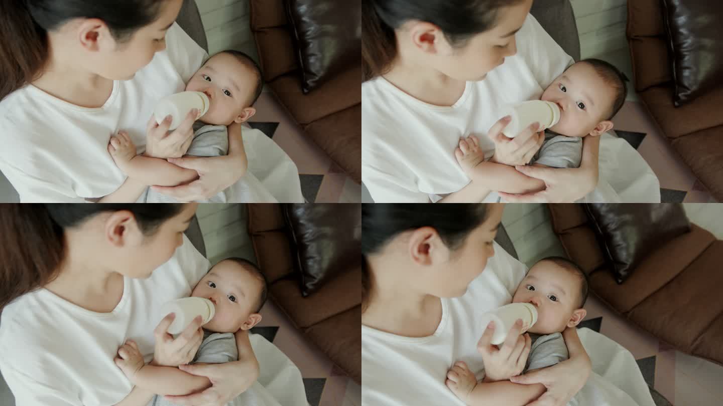 回头看：快乐单身母亲在家里的客厅里用奶瓶给亚洲男婴喂奶。