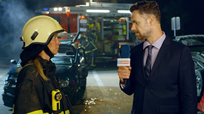 男性新闻记者在夜间车祸现场采访一名女性消防员