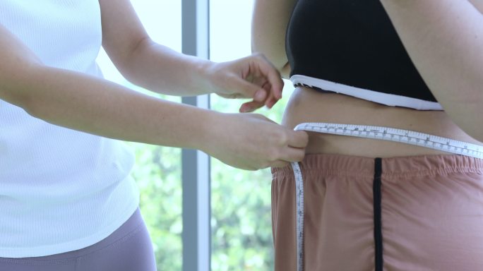 年轻的女教练测量身材高大的女性的大体型层，在健身时腰围