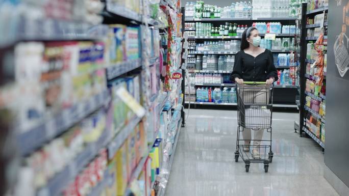 亚洲中年妇女在封锁后检查并阅读UHT牛奶标签，在超市或商店购物时戴上医用口罩以防冠状病毒大流行