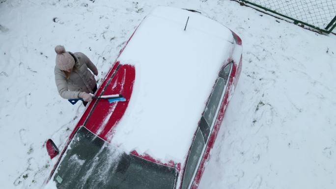 一名妇女正在清理车顶上的积雪