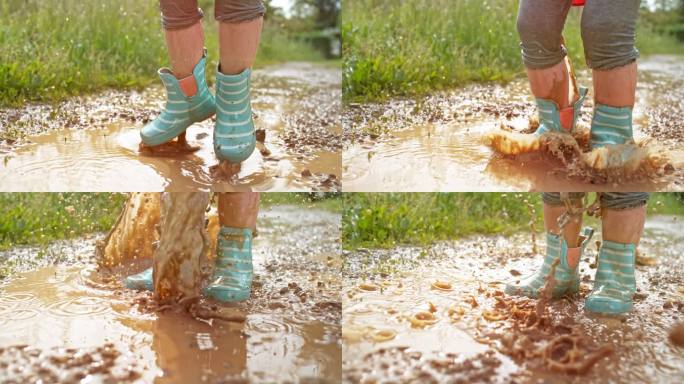 一个穿着雨靴和雨衣的小孩在泥泞的水坑里跳跃的腿