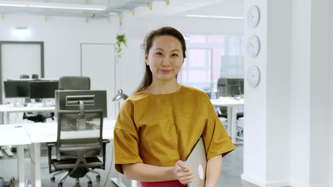 一位穿着便装、手持笔记本电脑站在办公室的亚洲女性的肖像