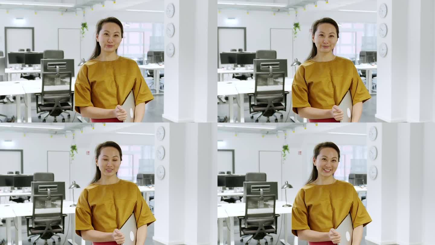 一位穿着便装、手持笔记本电脑站在办公室的亚洲女性的肖像