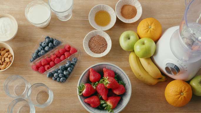 新鲜草莓、香蕉、青苹果杏仁、橙子的俯视图，以及用于制作健康奶昔的搅拌器，健康饮食和营养，碱性，素食理