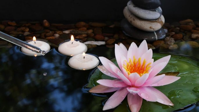 吸管中的油在平衡石、小蜡烛和粉色莲花附近掉入水中