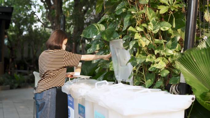 年轻的亚洲妇女在不同的垃圾桶里分类垃圾。