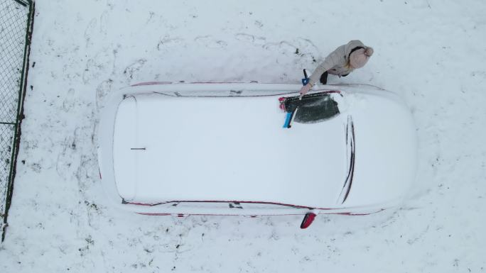鸟瞰图，一名妇女正在清理车上的积雪